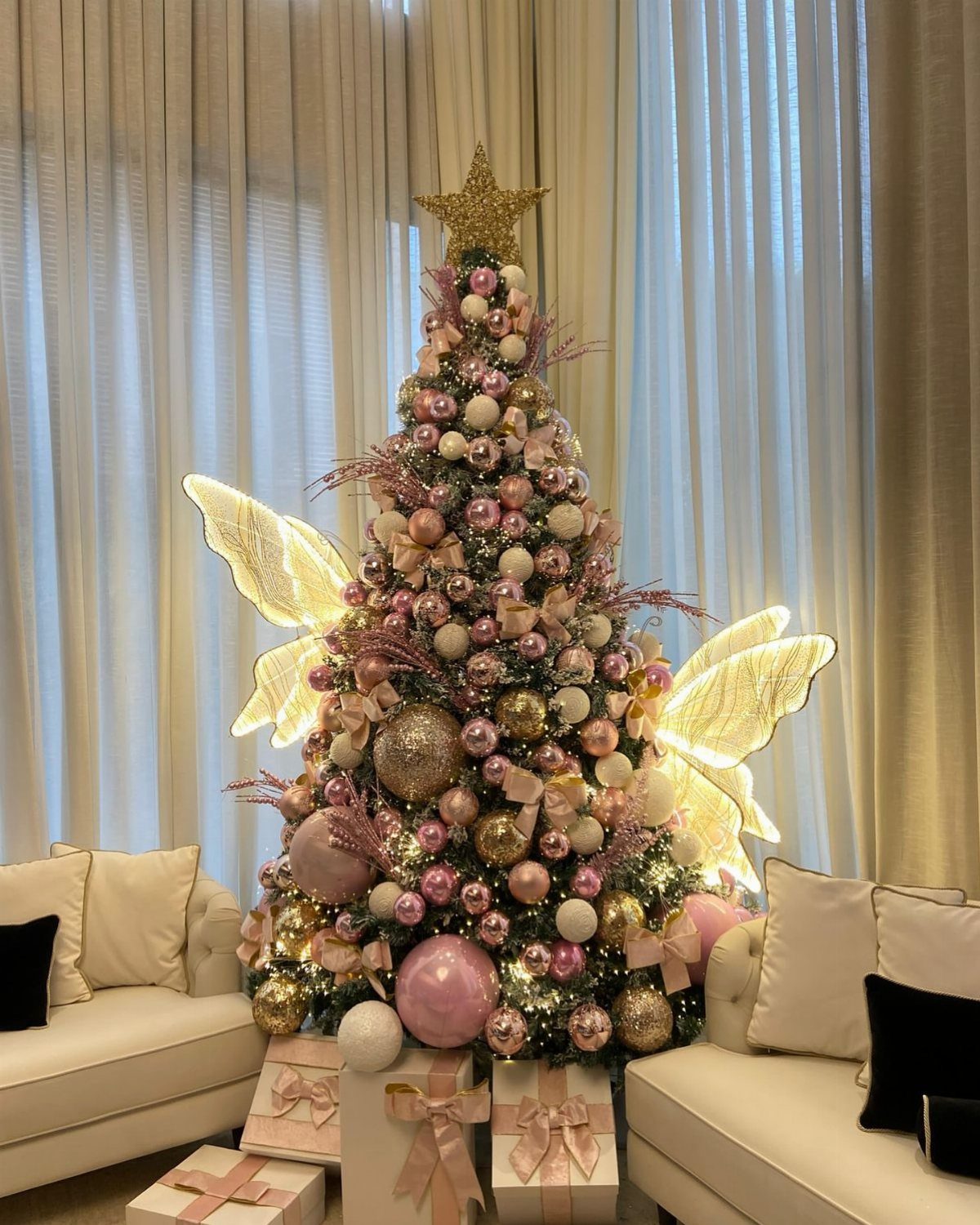 Opulent Christmas tree with pink and gold ornaments and glowing fairy wings behind it.