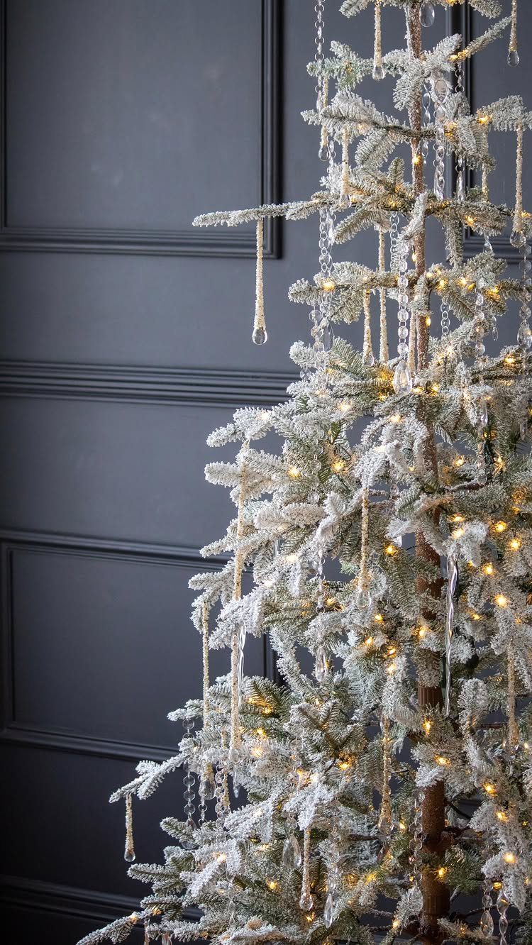 Flocked Christmas tree with warm lights and hanging glass icicles against dark walls