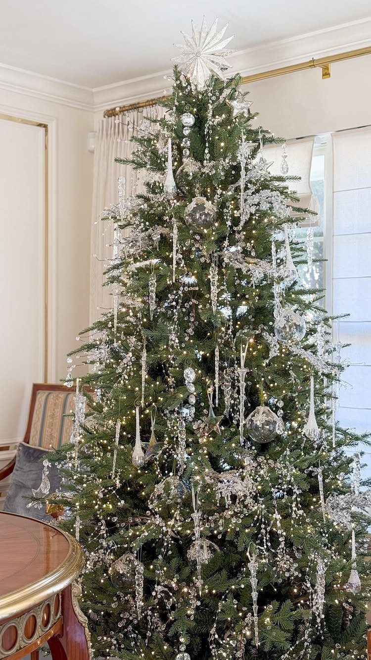 Green Christmas tree decorated with silver glass ornaments and warm white fairy lights.