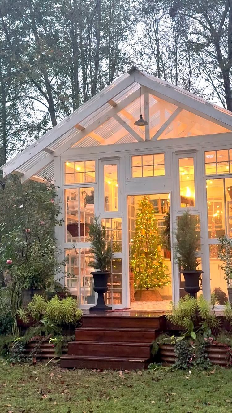 Glowing Christmas tree inside a white glass greenhouse surrounded by lush outdoor greenery