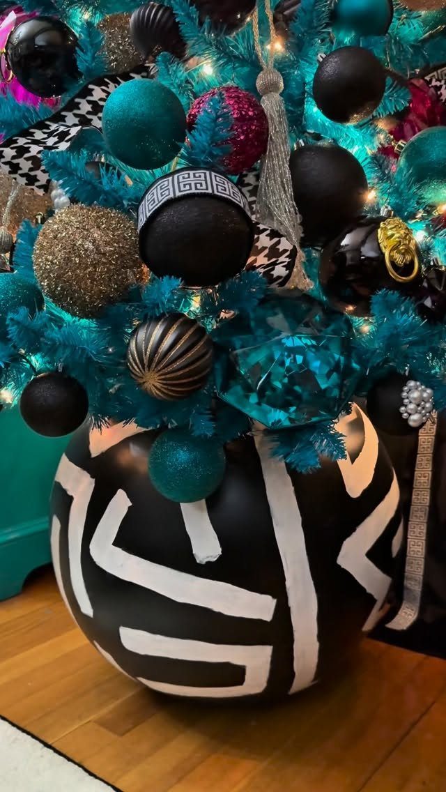 Teal Christmas tree decorated with black and gold ornaments and a large patterned ball.