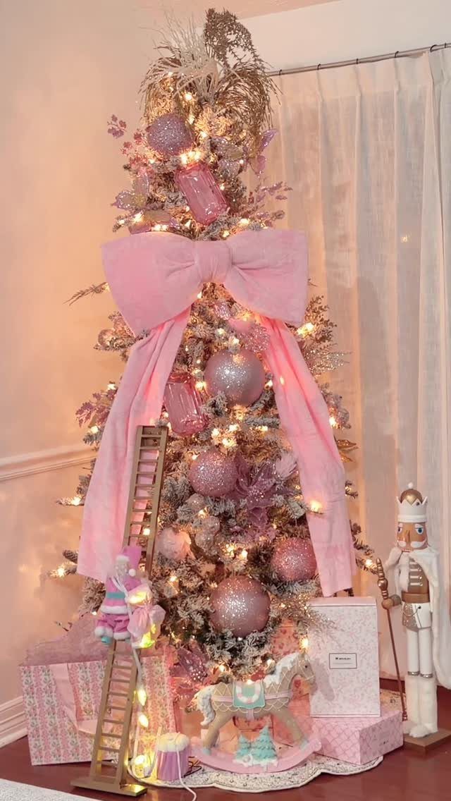 Flocked Christmas tree decorated with pink ornaments, a large pink bow, and warm lights.