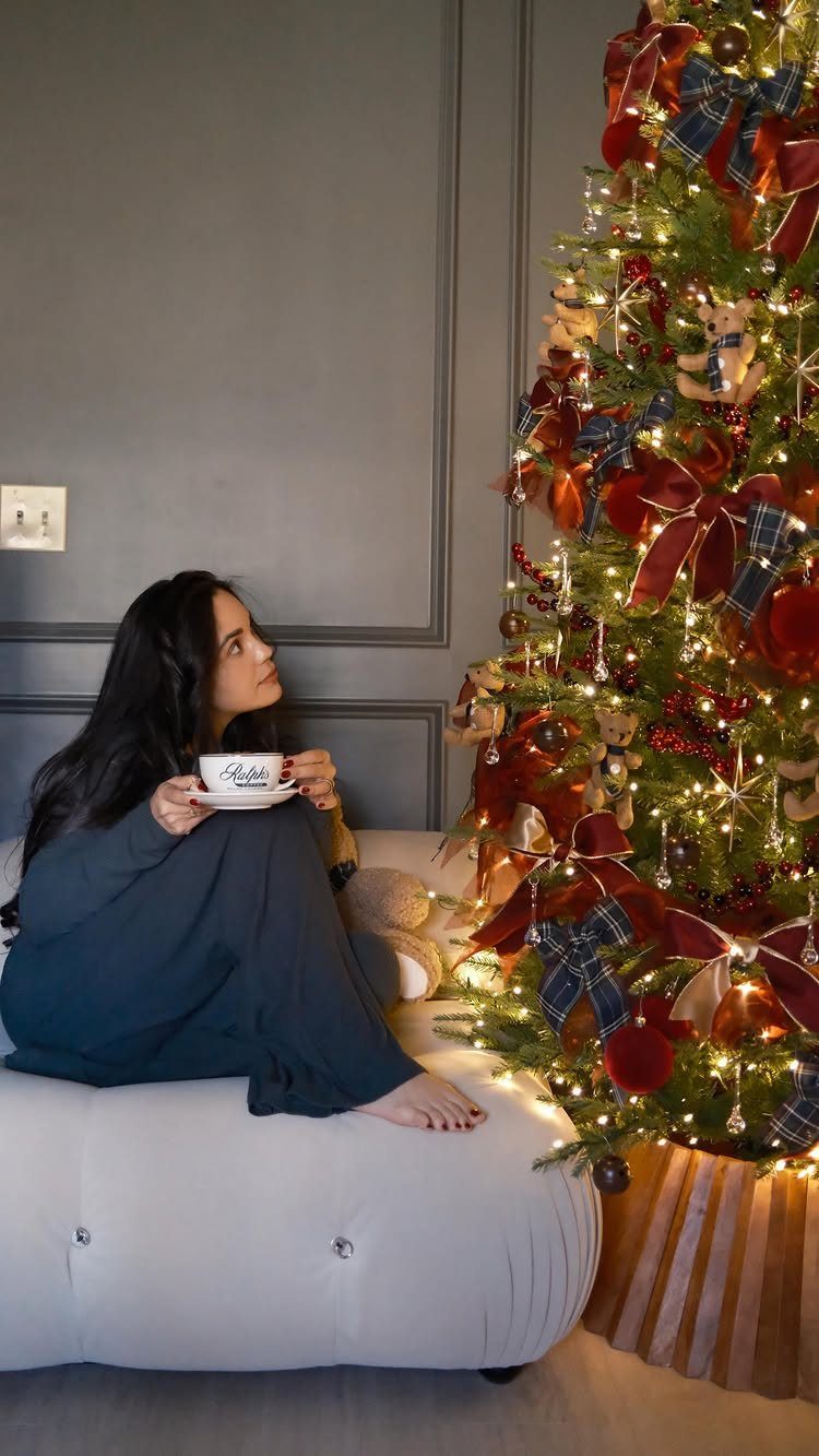 Woman sitting on a white sofa beside a Christmas tree decorated with plaid ribbons.