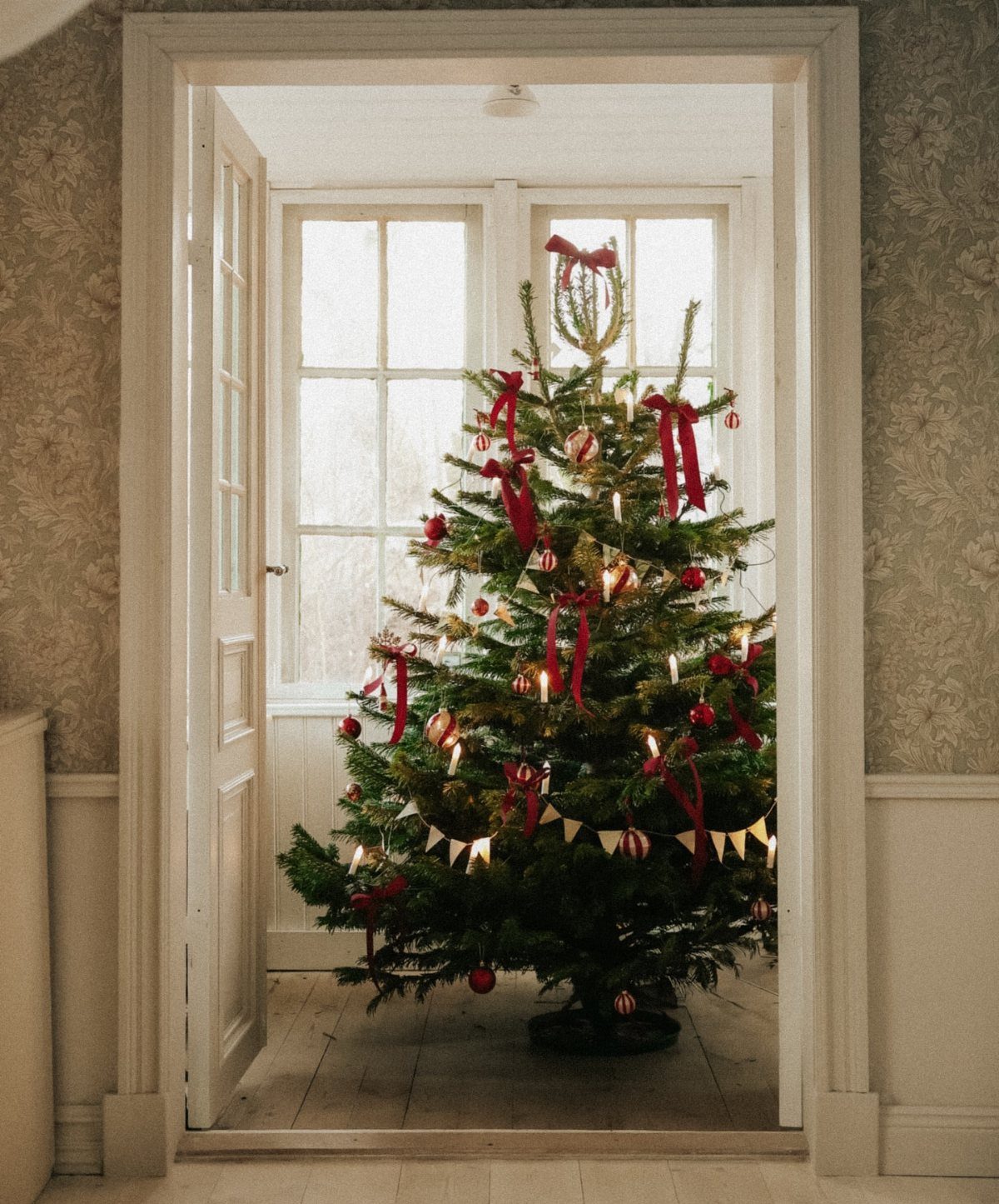 Decorated fir Christmas tree with red ribbons and candles in a bright room