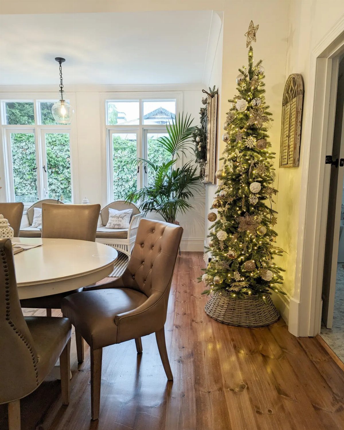 Tall slender Christmas tree with gold ornaments in a bright dining room