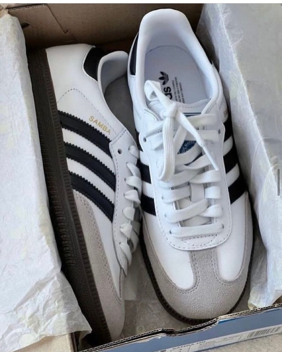 White Adidas Samba OG sneakers with black stripes inside a cardboard shoebox.