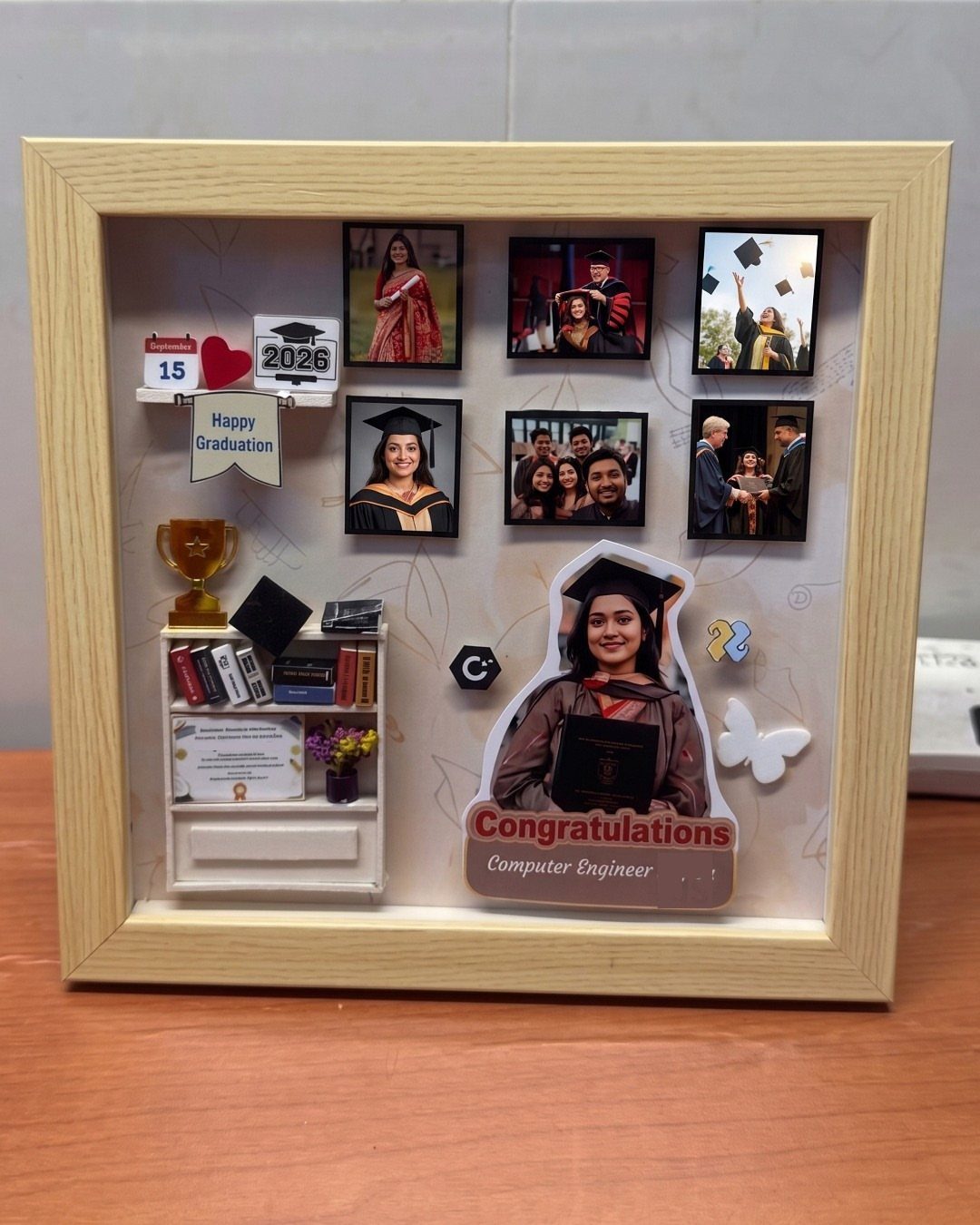 Shadow box frame with graduation photos, miniature bookshelf, and congratulations message.