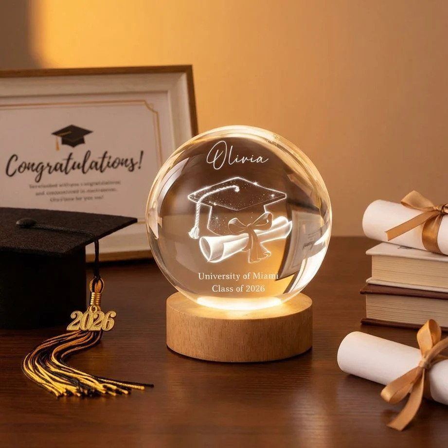 Engraved glass graduation sphere on wooden base with cap and diploma scrolls