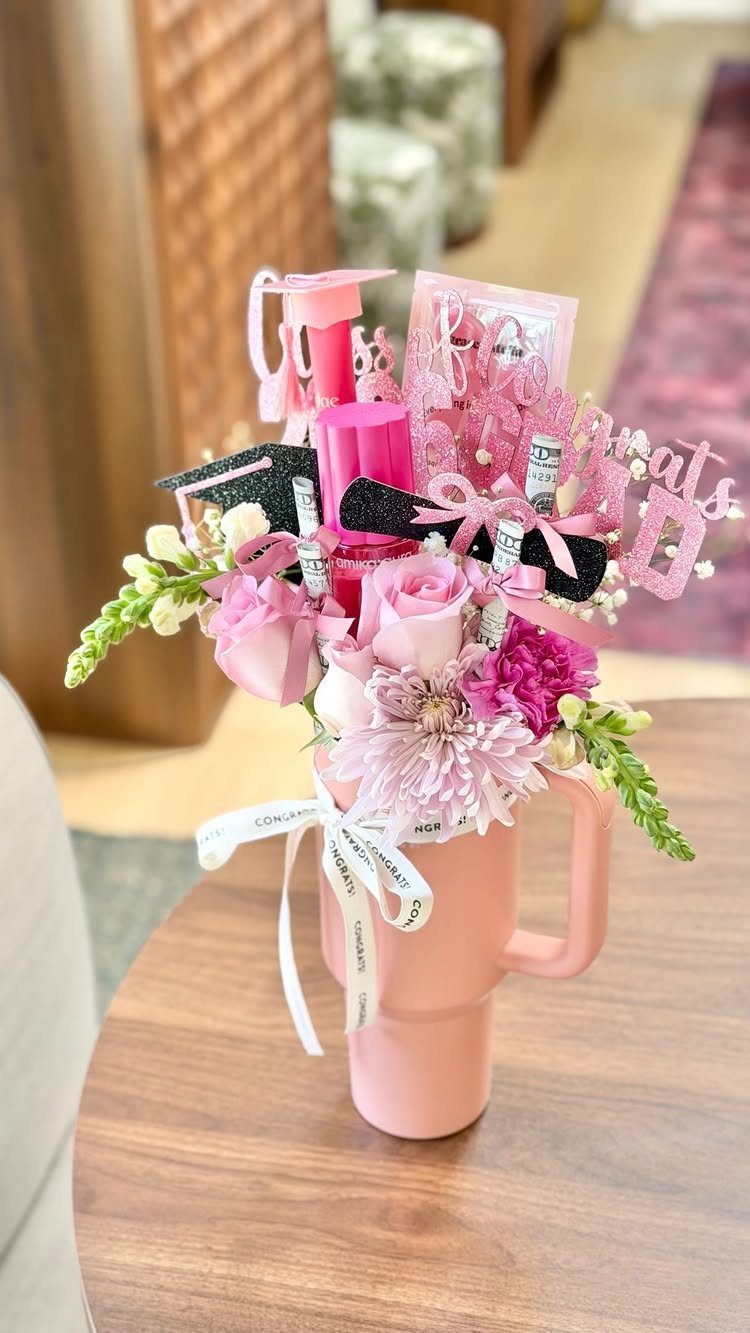 Pink graduation gift arrangement with flowers and makeup in a pink mug.