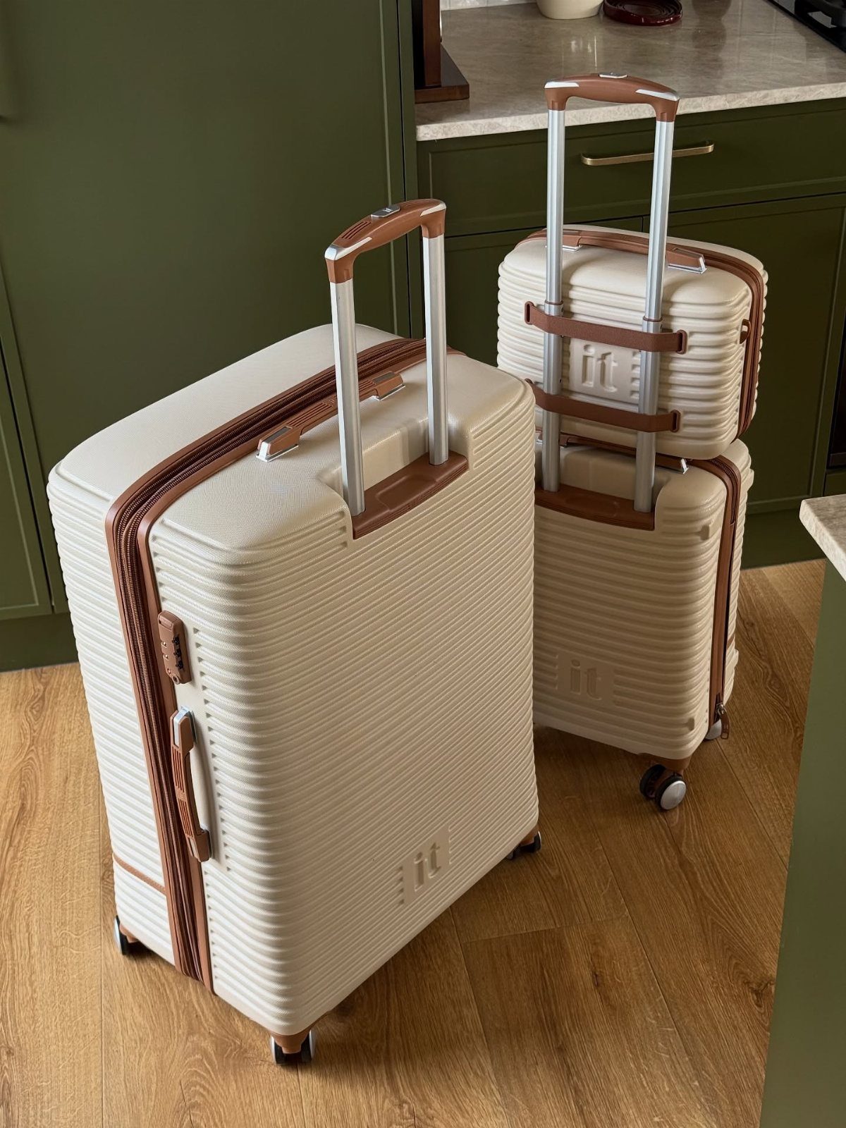 Two cream hardshell suitcases with brown leather straps on a wooden floor.
