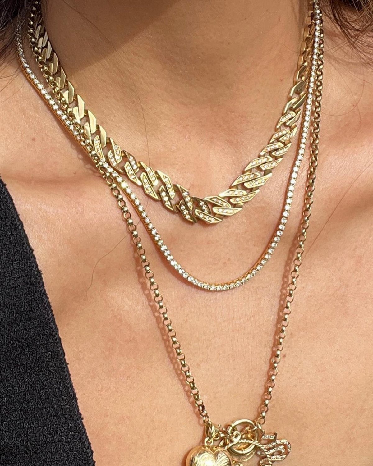Layered gold necklaces including a curb chain and heart pendant on a person.
