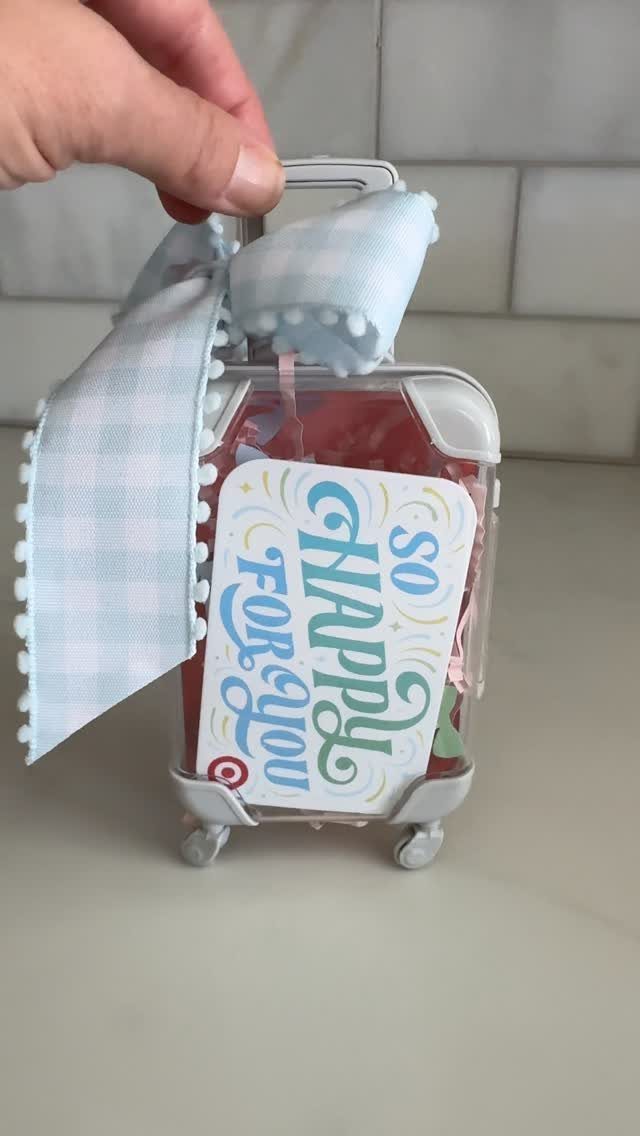 Clear suitcase-shaped gift box with blue gingham ribbon and celebratory card.