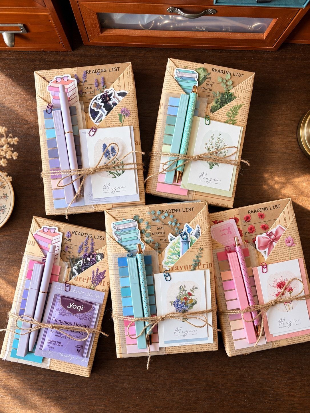 Five tan notebooks bundled with twine, pencils, and floral cards on wood.
