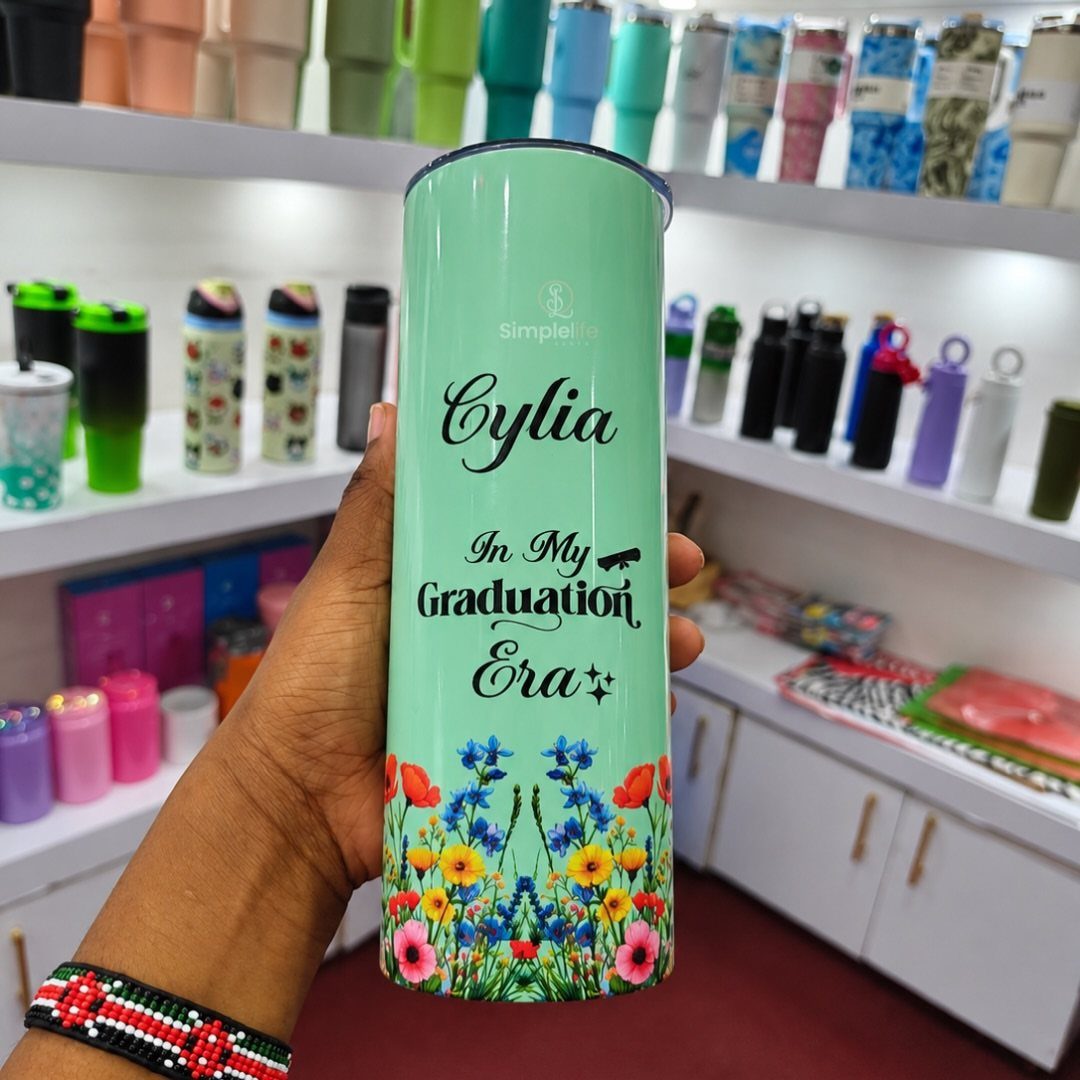 Light-green insulated tumbler with graduation text and flowers held by a hand.