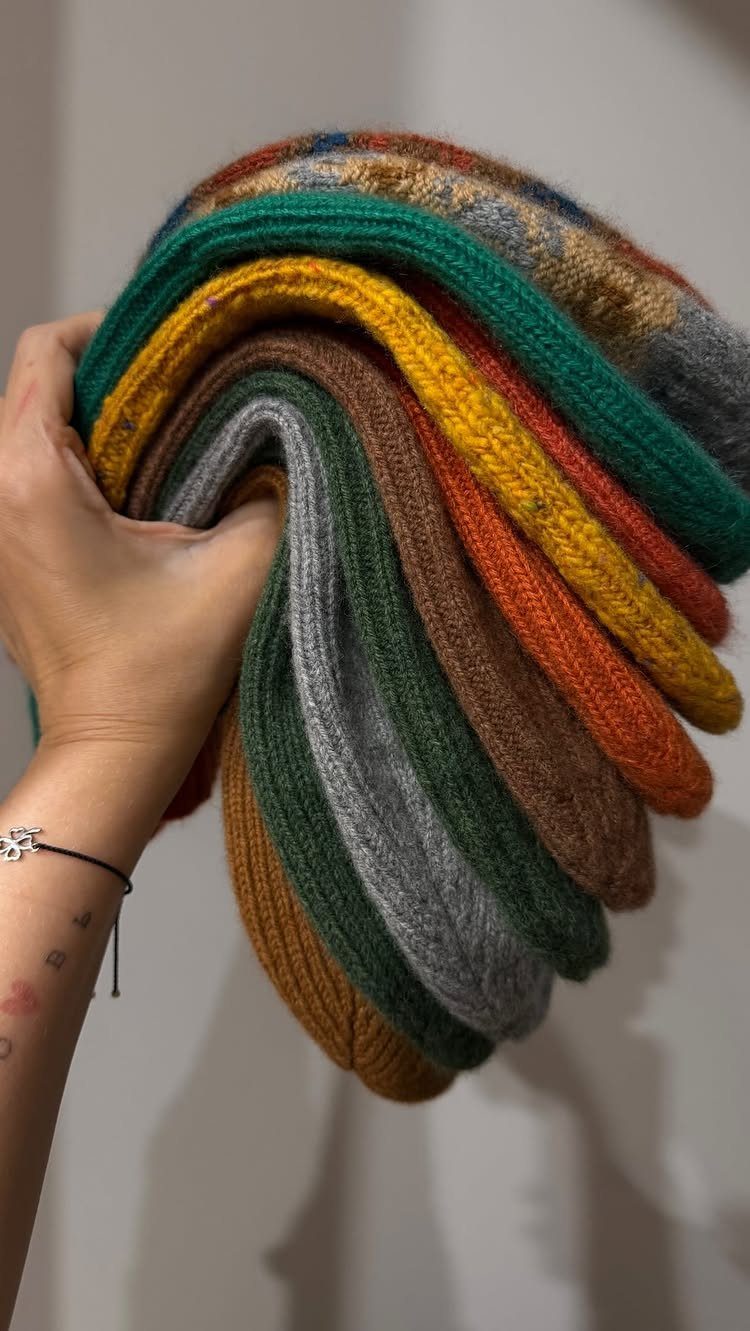 Hand holding a colorful stack of folded wool socks in earthy tones.