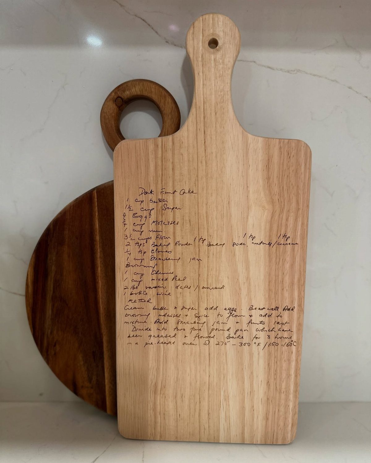 Engraved wooden cutting board with a handwritten recipe leaning against a round board.