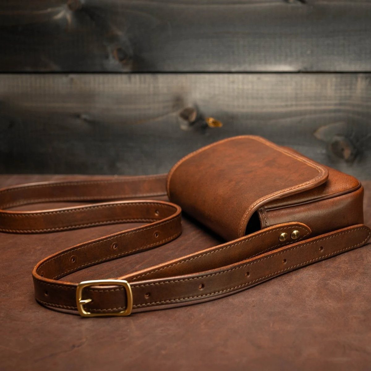 Brown leather messenger bag with gold buckle on a dark wooden background