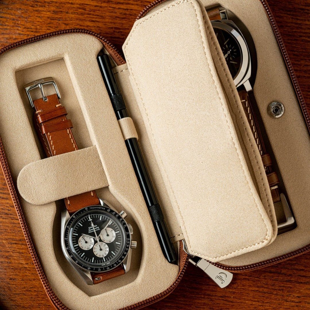Leather watch case holding two wristwatches and a pen on a wooden table