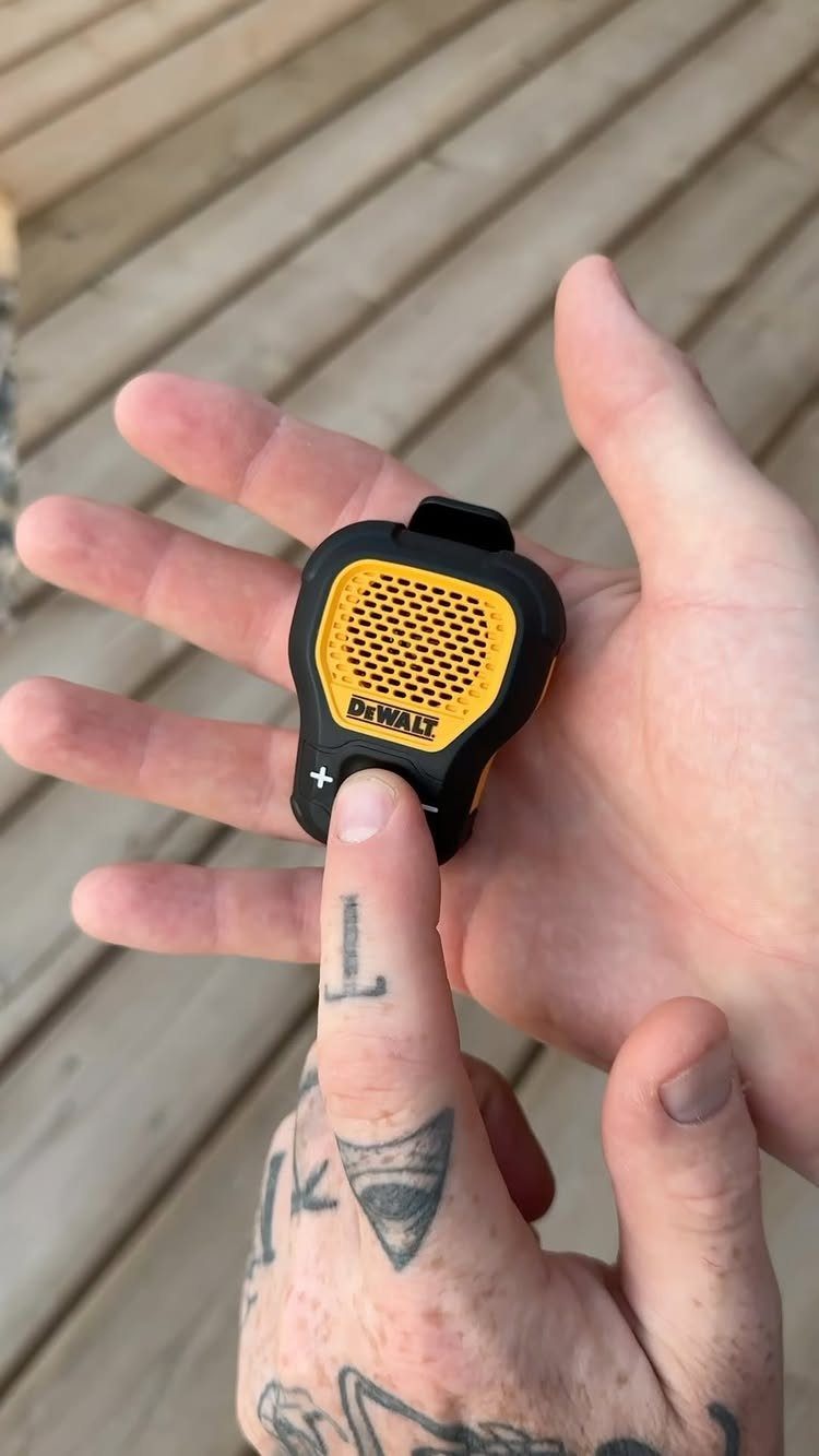 Small yellow and black DeWalt portable Bluetooth speaker held in a tattooed hand.