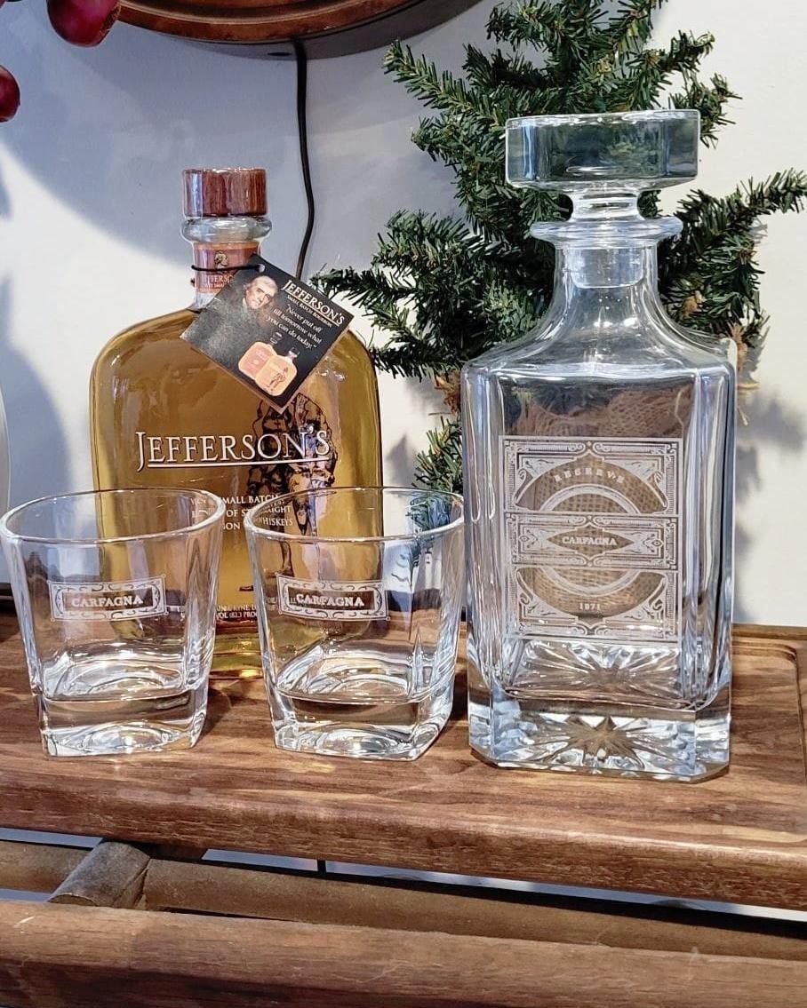 Whiskey bottle, etched glass decanter, and two matching glasses on a wooden table.