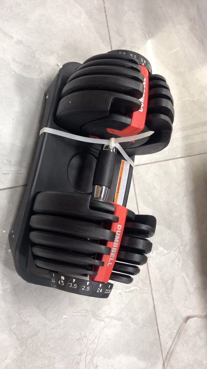 Adjustable black and red dumbbell resting on a light grey marbled floor.