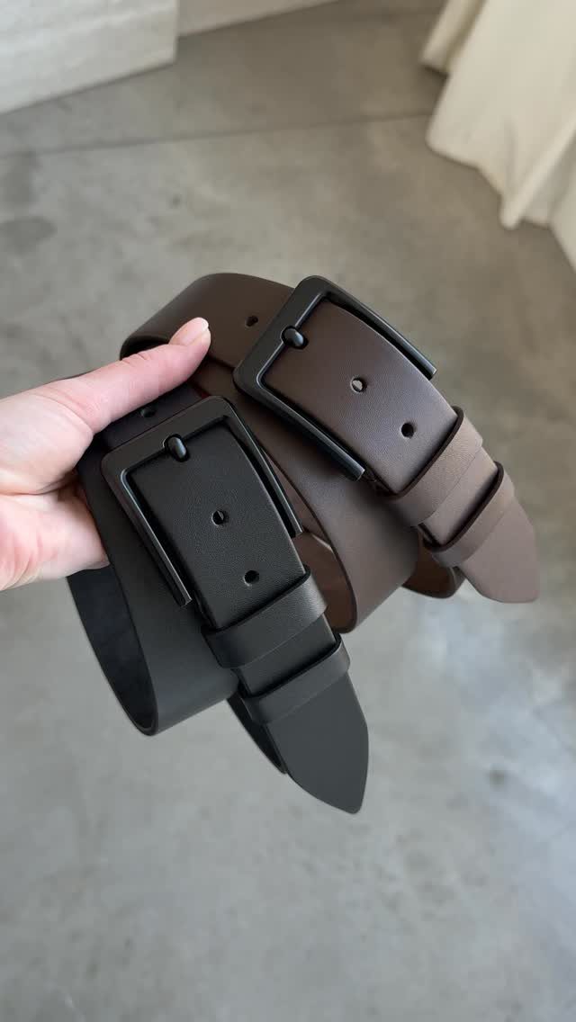 Two leather belts, one black and one brown, held by a hand.