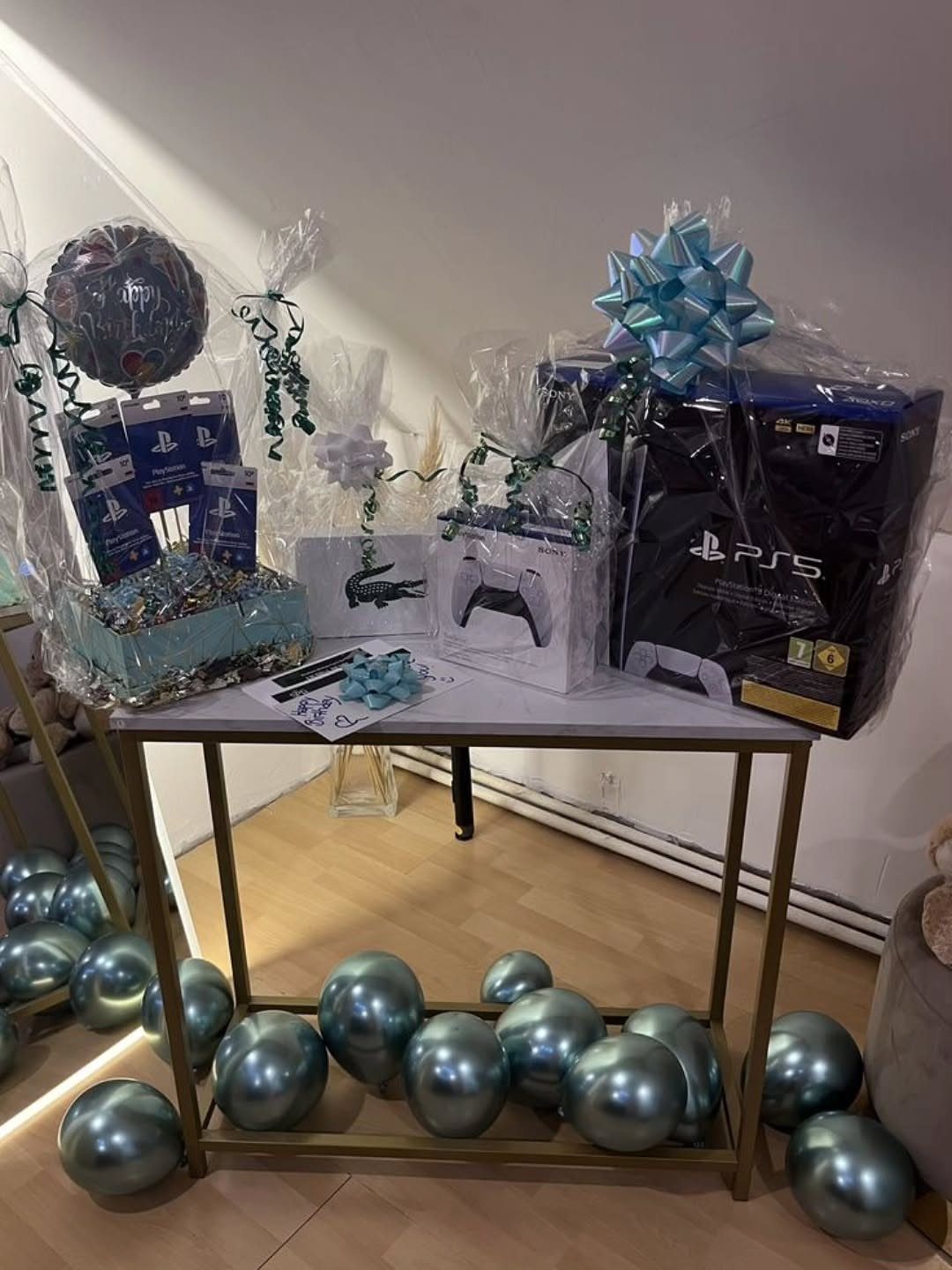 PlayStation 5 console and accessories wrapped as gifts on a table with blue balloons.