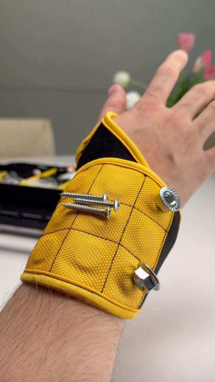 Yellow magnetic tool wristband holding metal screws and nuts on a person's arm