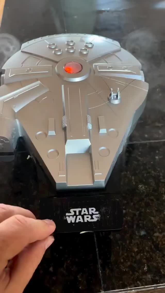 Silver Millennium Falcon model on a black Star Wars branded display stand.