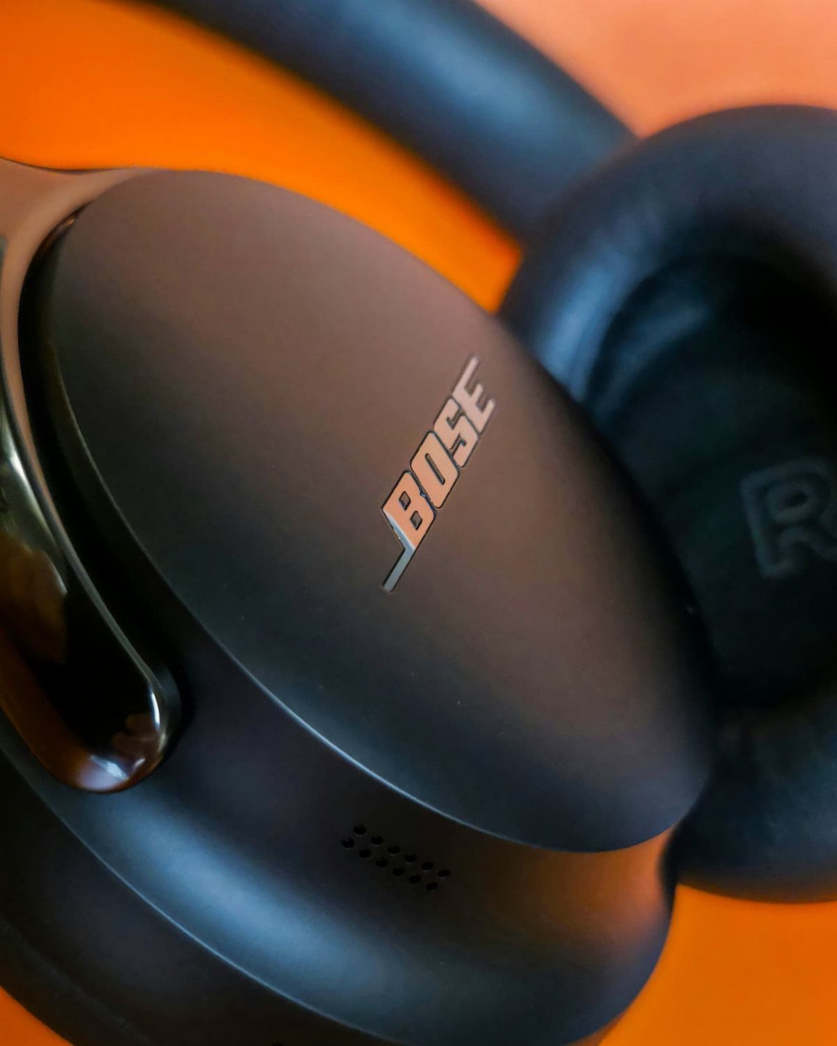 Black Bose over-ear headphones resting on a bright orange background.