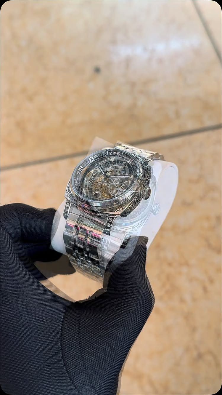 Silver skeleton wristwatch wrapped in plastic held by a black gloved hand