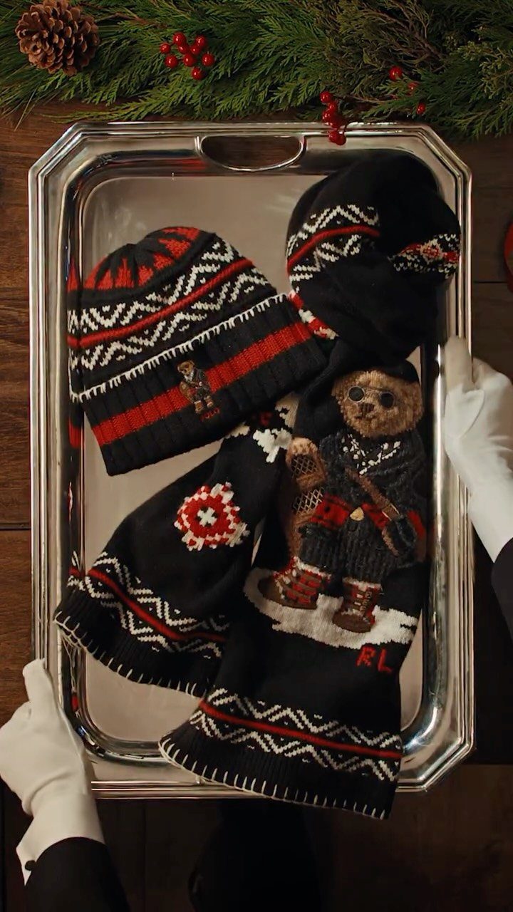 Knit beanie, scarf, and teddy bear on a silver tray with holiday greenery.