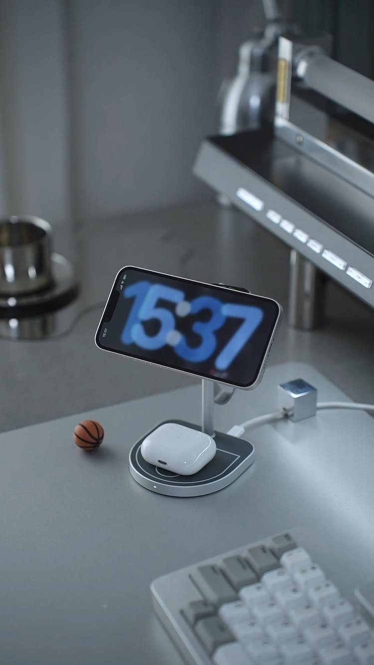 Wireless charging station holding a smartphone and wireless earbuds on a grey desk
