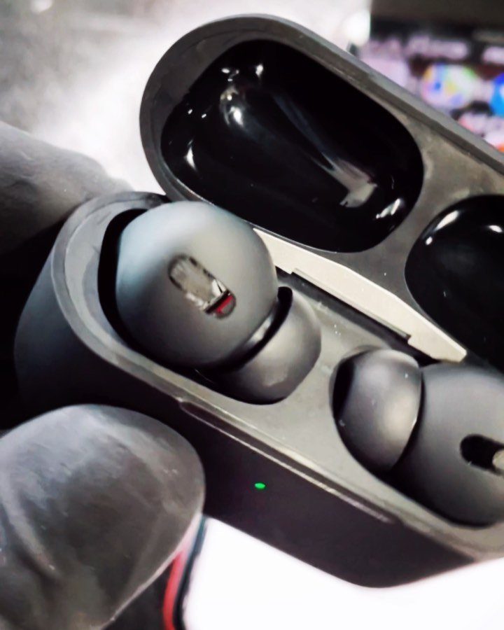 Black wireless earbuds inside an open black charging case held by gloved hands