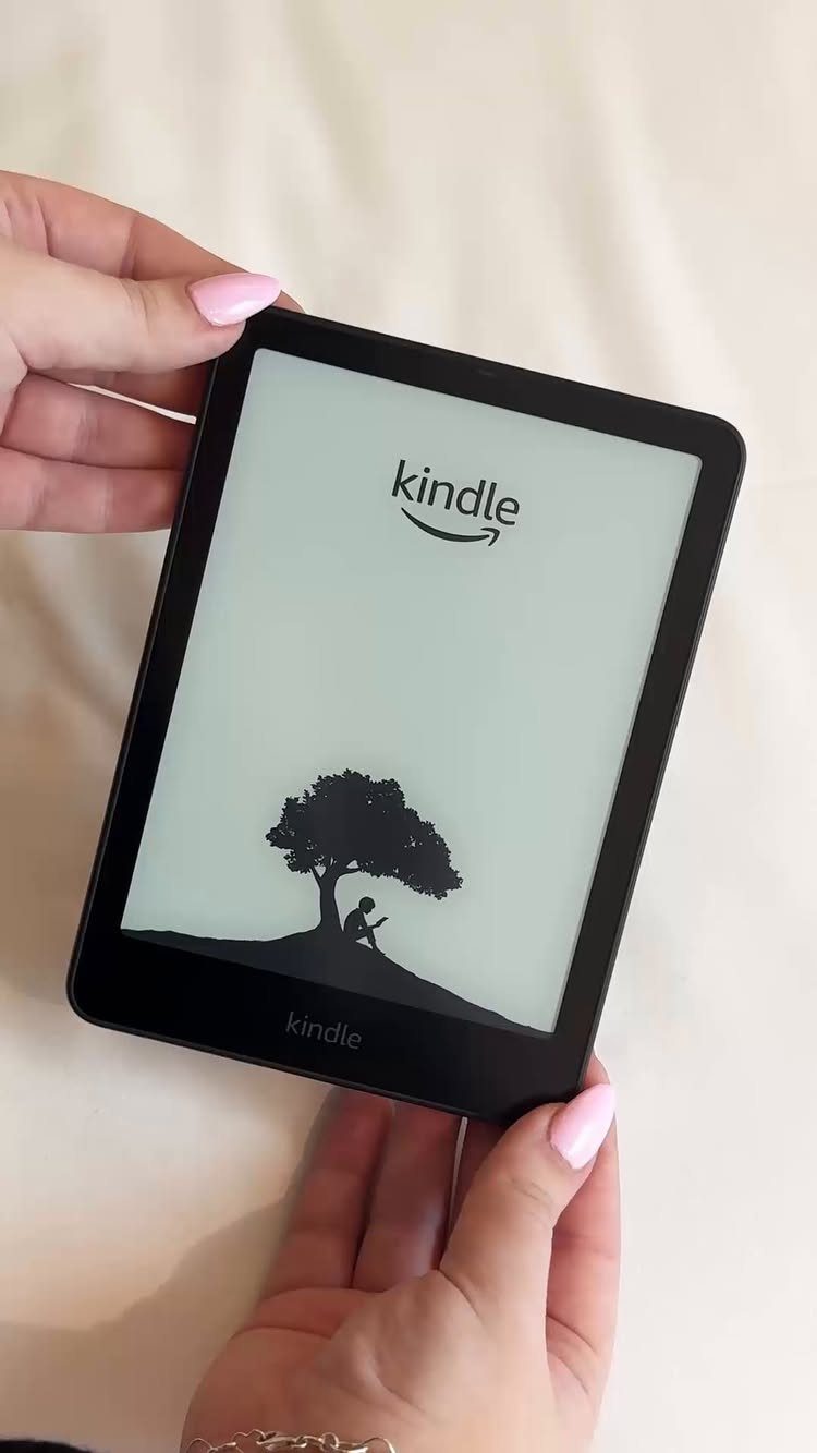 Hands holding a black Kindle e-reader showing the logo and a tree silhouette.