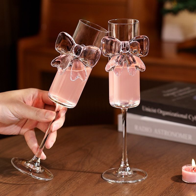 Two elegant champagne flutes with decorative glass bows filled with pink liquid.