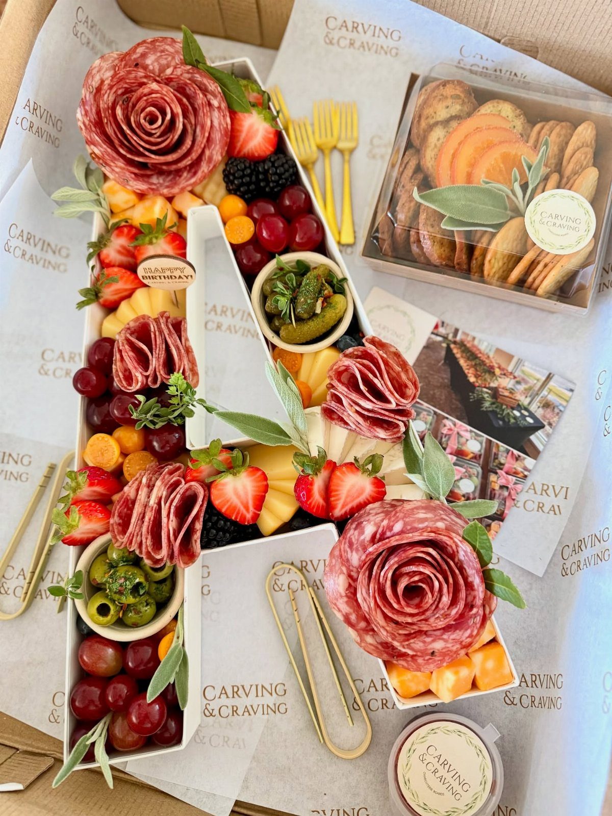 Letter A shaped cheese board filled with salami roses, fruits, and olives