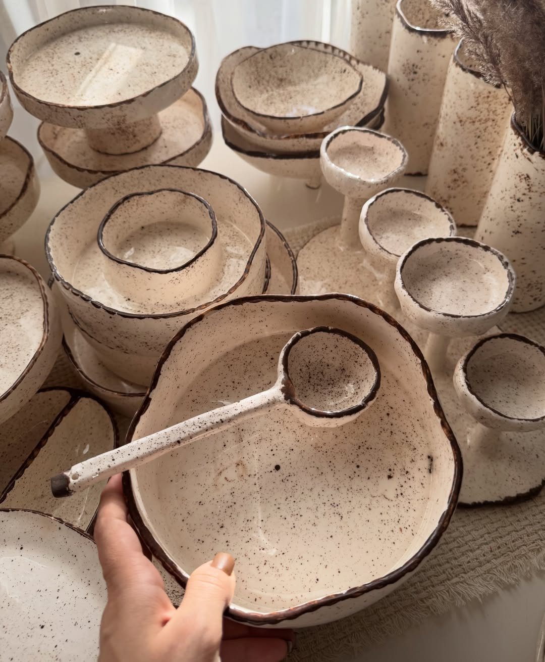 Handmade speckled ceramic bowls and a spoon in a neutral off-white tone.