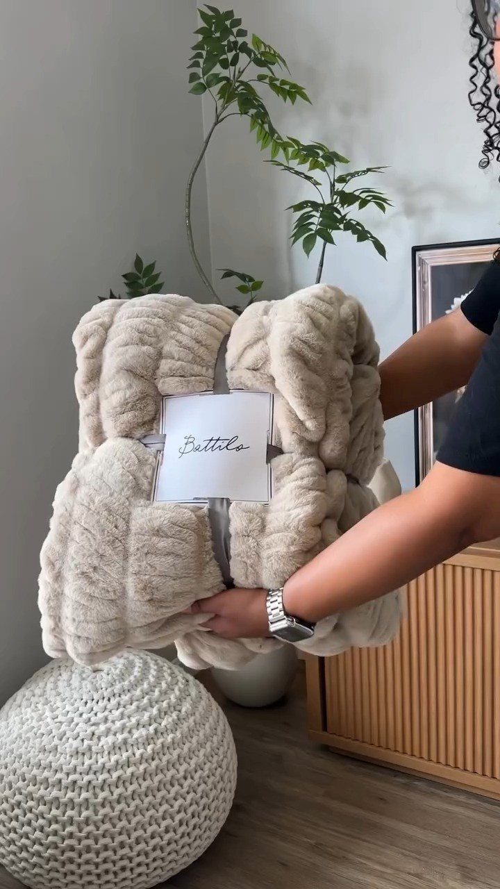 Cream-colored plush faux fur throw blanket held by hands in a modern living room