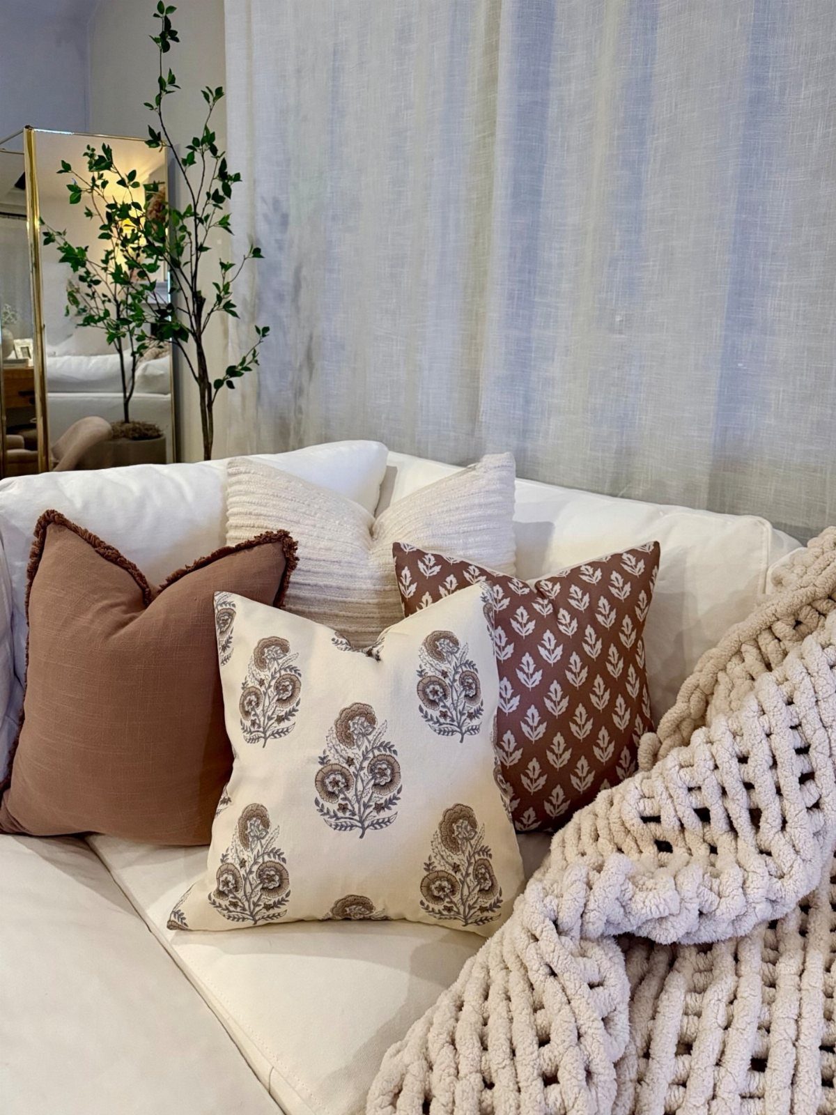 Decorative throw pillows in brown and cream patterns on a white sofa with blanket.
