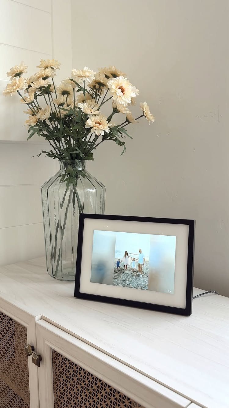 Digital photo frame showing a family on a beach next to cream flowers.