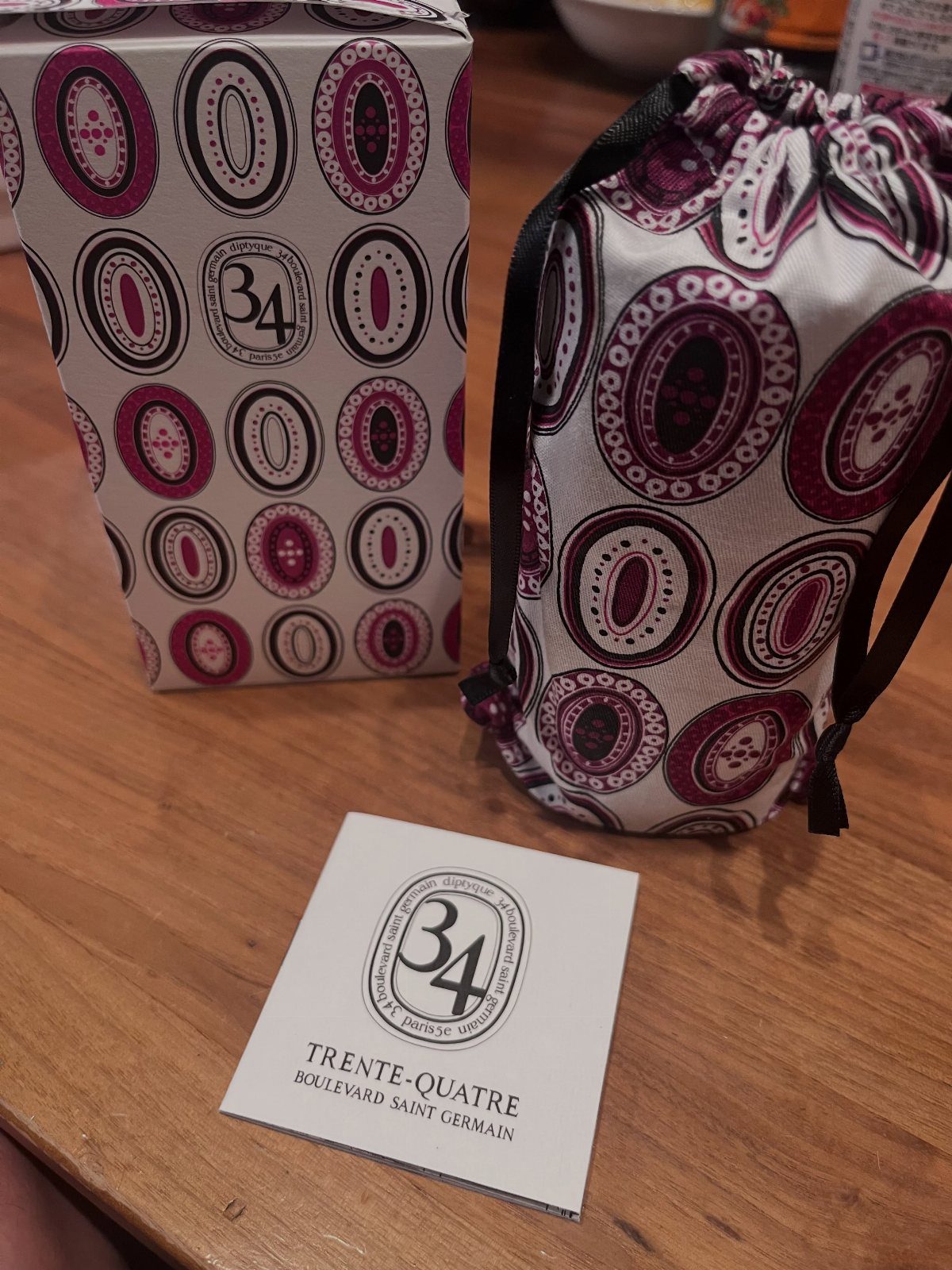 Diptyque 34 Boulevard Saint Germain candle packaging, fabric bag, and logo card on wood.