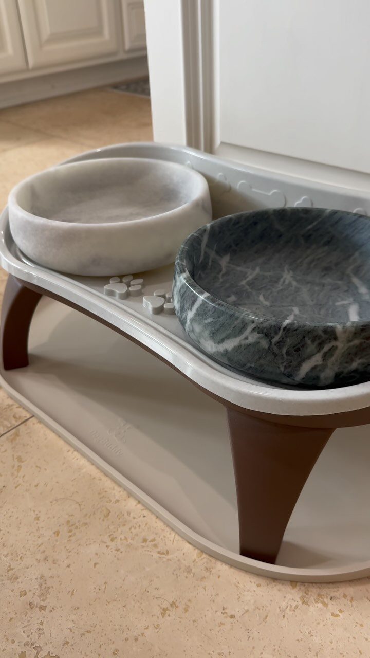 Two marble pet bowls on an elevated white and brown stand on tiled floor.