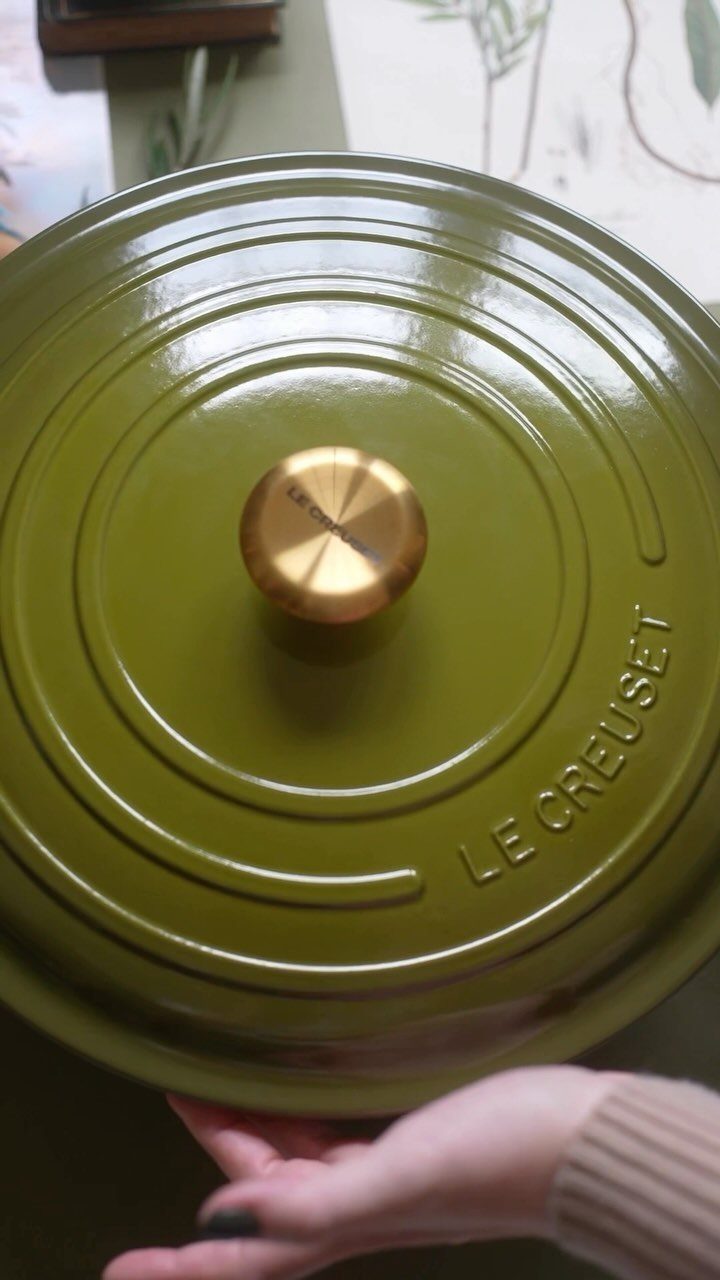 Green Le Creuset cast iron pot lid with a gold knob held by hand.