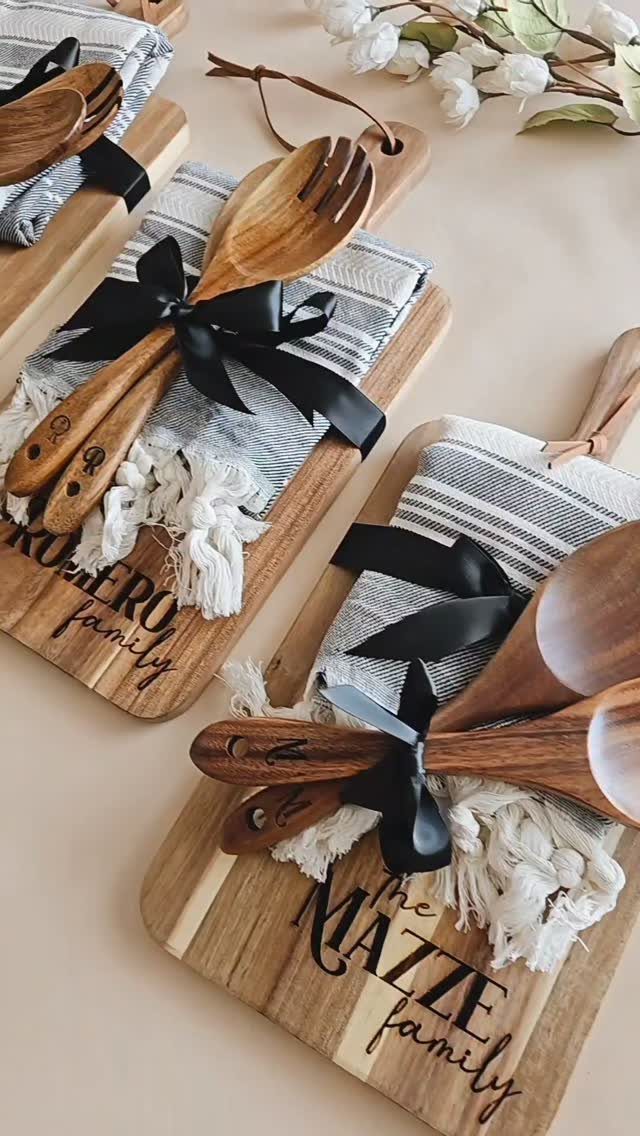 Personalized wooden serving boards bundled with striped towels and wooden utensils with black ribbons.