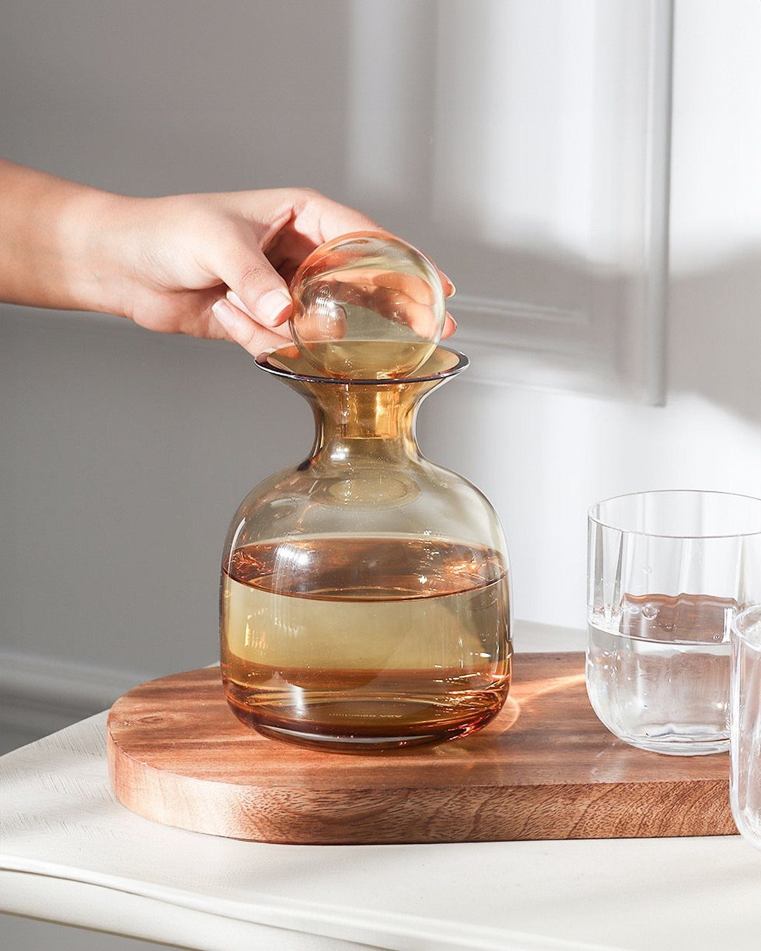 Brown glass water carafe with a round stopper on a wooden board.
