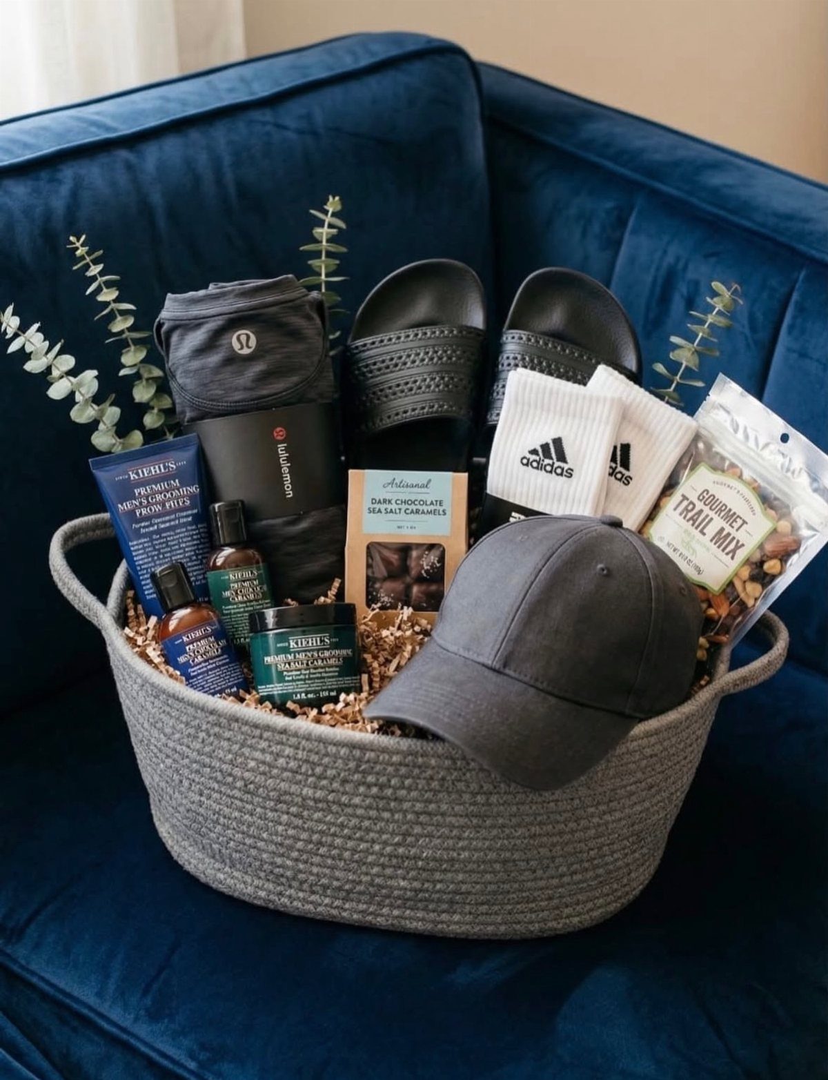 Grey woven gift basket with athletic wear, grooming products, and snacks on blue sofa