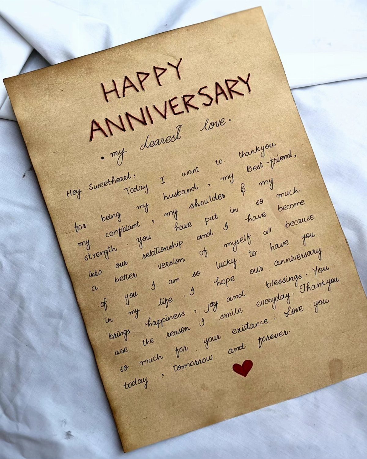 Handwritten anniversary letter on brown parchment paper with a small red heart.