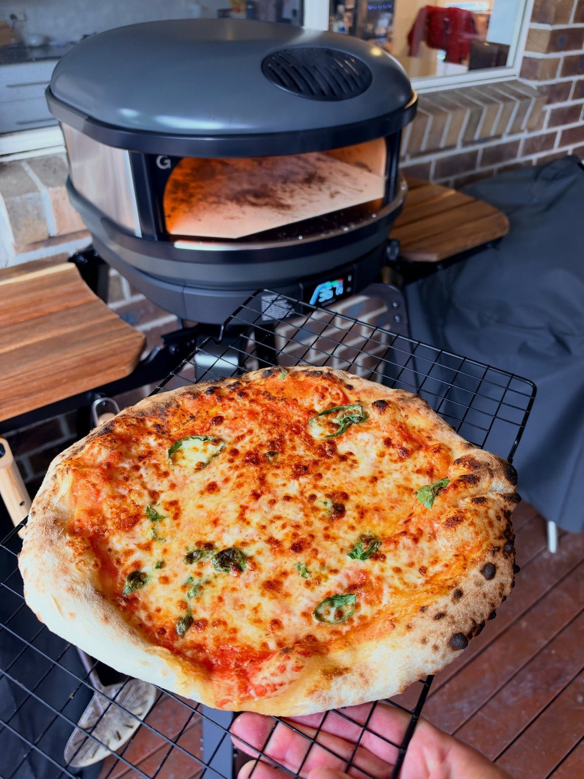 Freshly baked pizza on a wire rack in front of a portable pizza oven.