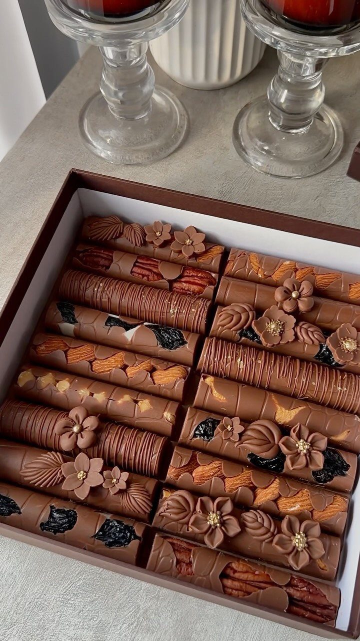 Assorted gourmet chocolate cylinders with floral decorations in a brown gift box.